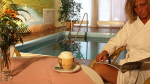 A person in a white bathrobe sitting by a pool with a cup of coffee and a book. - Landgasthof Hotel Hanses-Bräutigam (Schmallenberg)