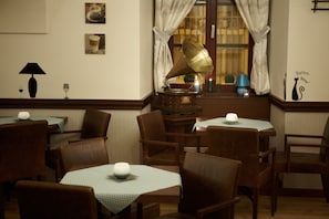 A cozy dining area with wooden tables and chairs, a gramophone, and wall decorations including framed pictures and a cat silhouette.