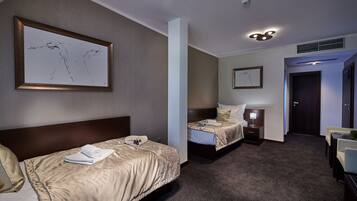 A hotel room with two beds, a large framed artwork on the wall, a ceiling light, and a door leading to another room.