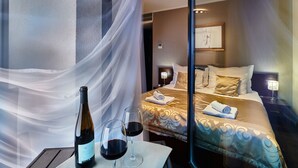 A hotel room with a bed, a table with a bottle and glasses, and a nightstand with a lamp. - Boutique Hotel Chrysso (Kosice)