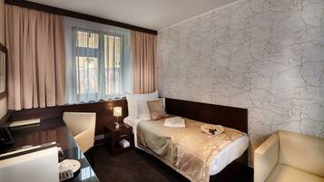 A hotel room with a bed, two chairs, a desk, a lamp, and a window with curtains.