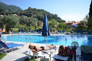 A poolside area with lounge chairs, umbrellas, and a clear view of the surrounding greenery and buildings. - Irene Apartments (Corfu)