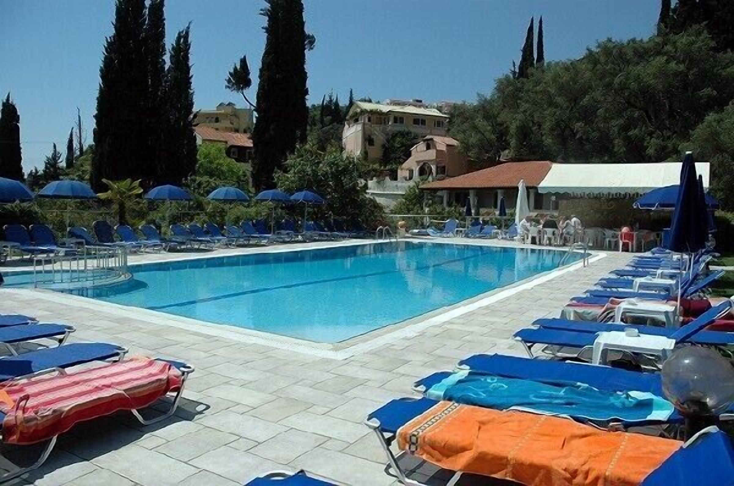 Une piscine entourée d’arbres et d’immeubles, avec des chaises longues et des parasols.