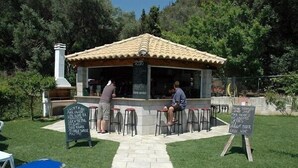 Un petit bar en plein air avec un toit recouvert de tuiles, un tableau noir servant de menu et des tabourets.