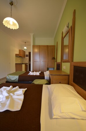 Habitación de hotel con dos camas, un armario de madera, una pequeña cocina y una lámpara colgante.