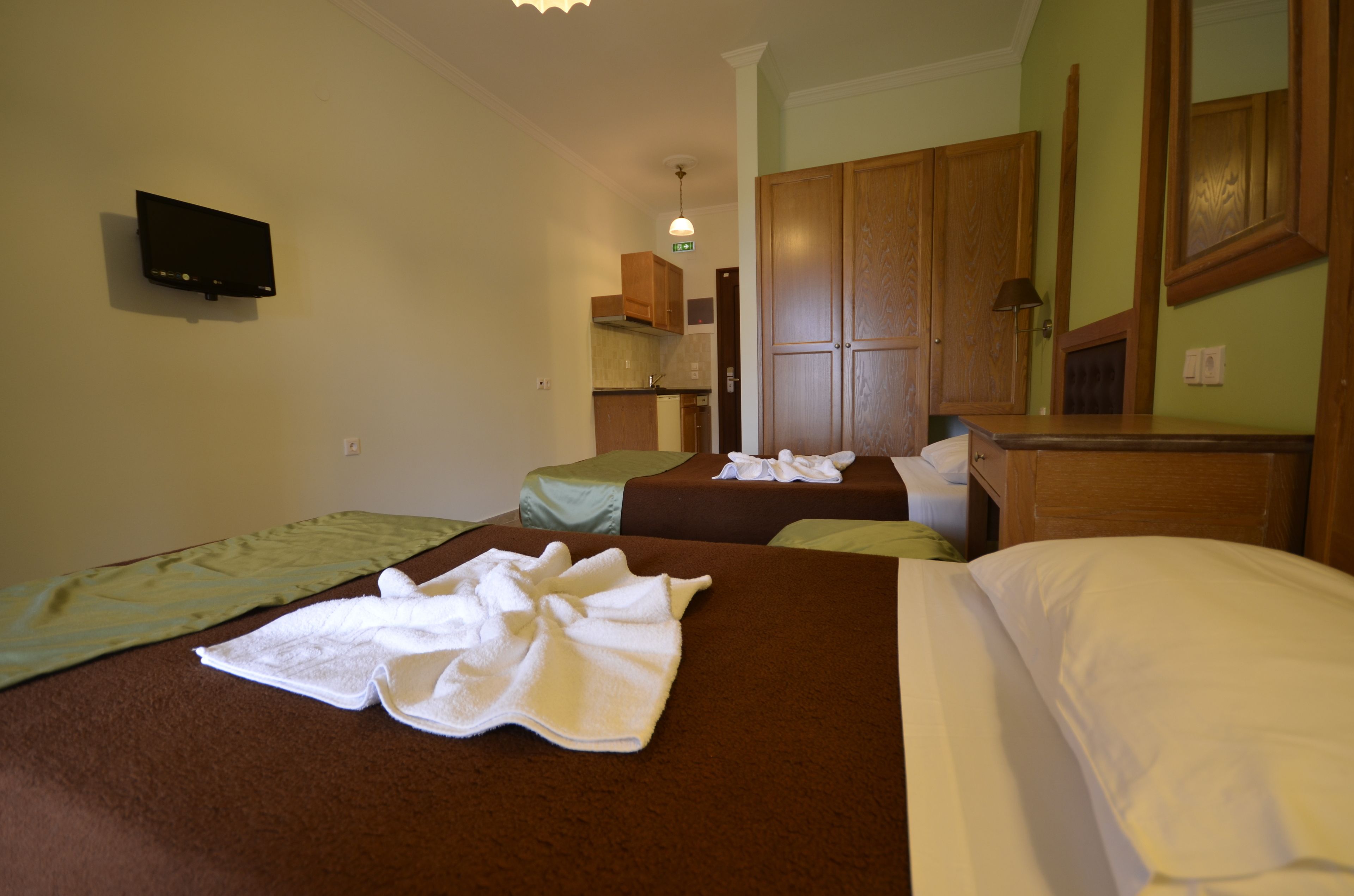 Habitación de hotel con dos camas, televisor, kitchenette y armarios de madera.