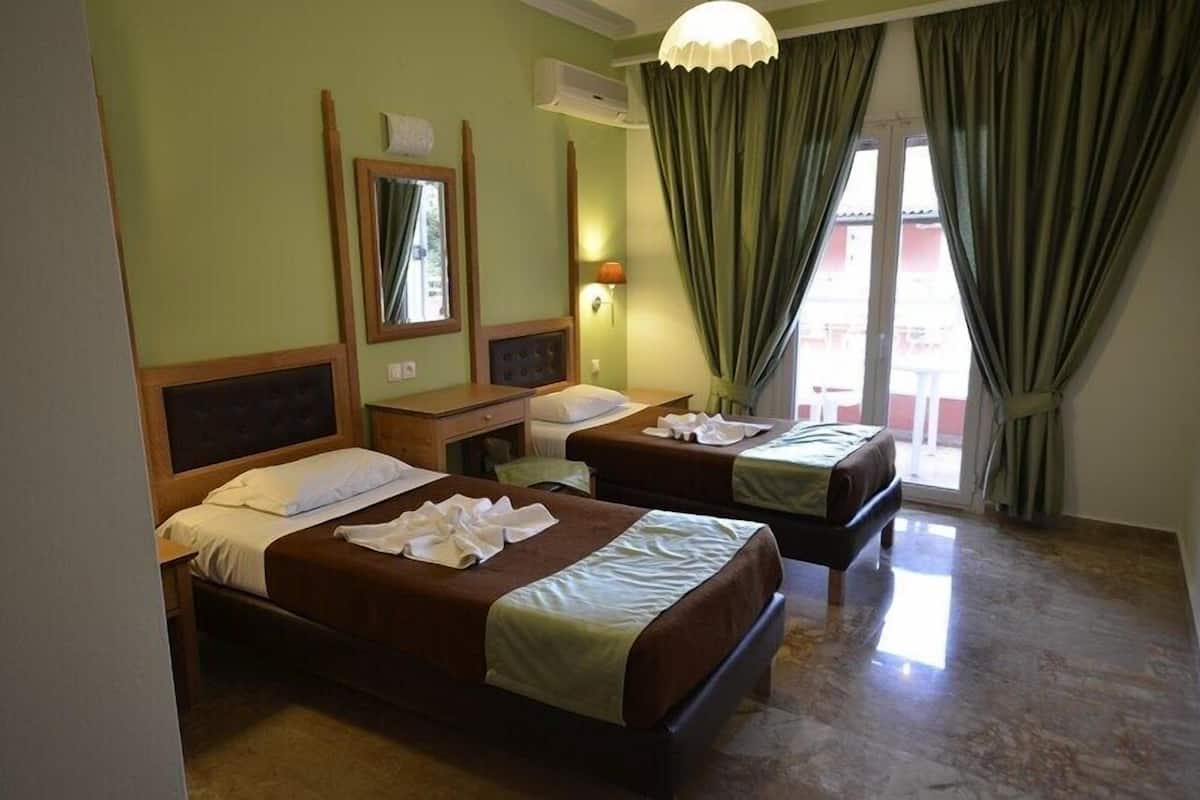 A hotel room with two beds, a desk, a mirror, and a window with curtains.