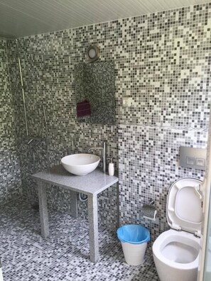 Un baño con pared de mosaicos, un lavamanos blanco y un inodoro.