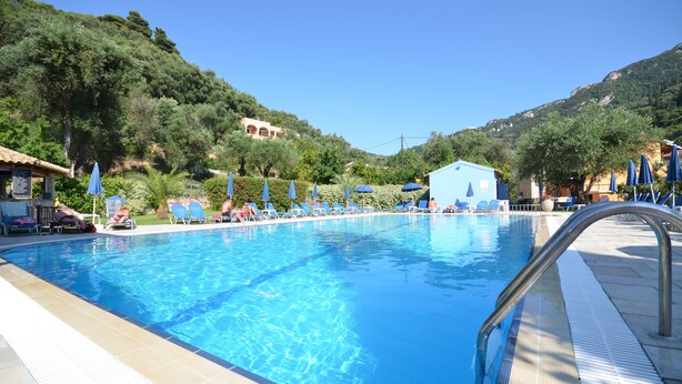 Une piscine entourée de verdure et de collines, avec des chaises longues et des parasols.