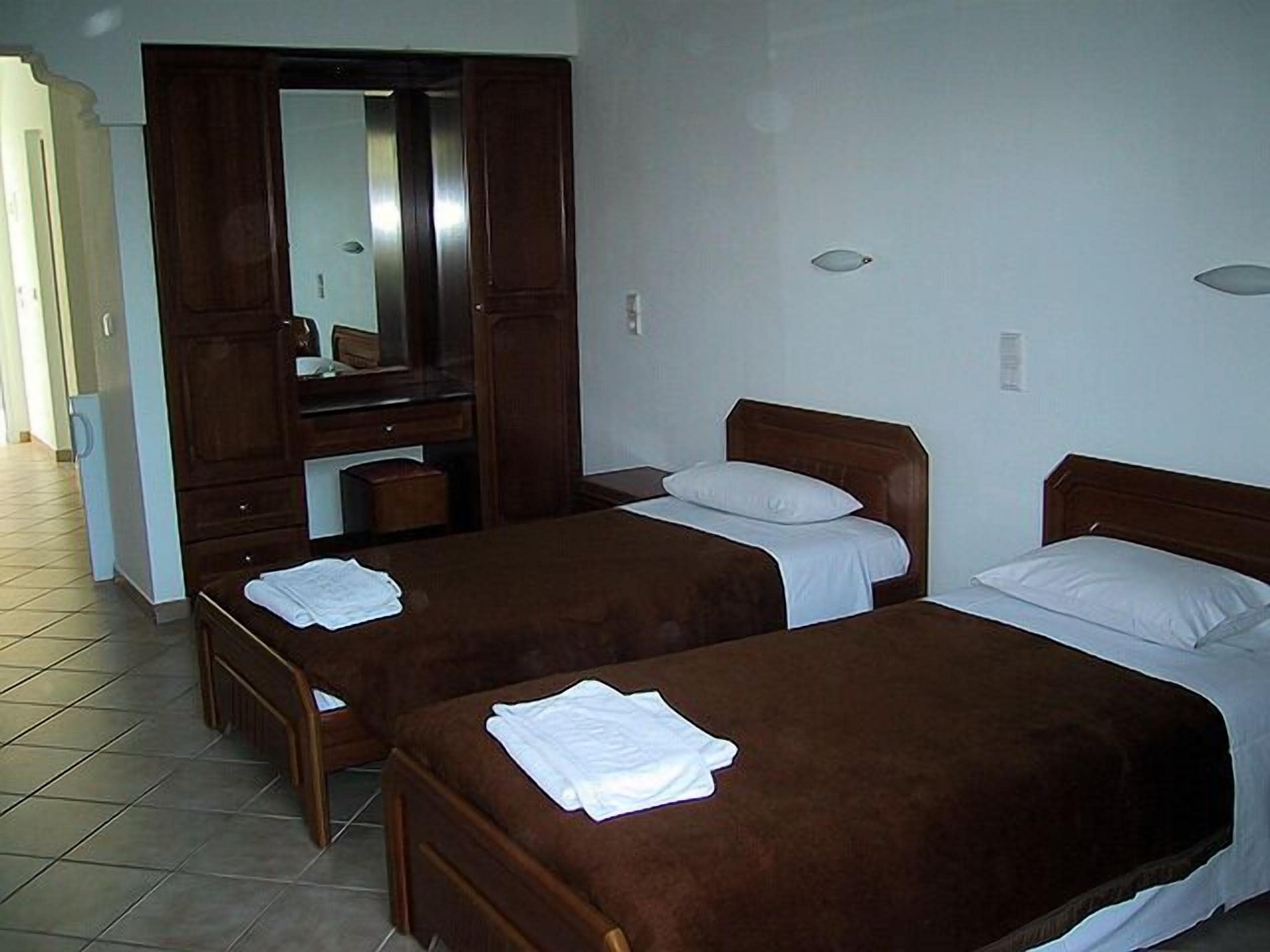 Ein Hotelzimmer mit zwei Einzelbetten, einem Holzschrank, einem Spiegel und einem gefliesten Boden.