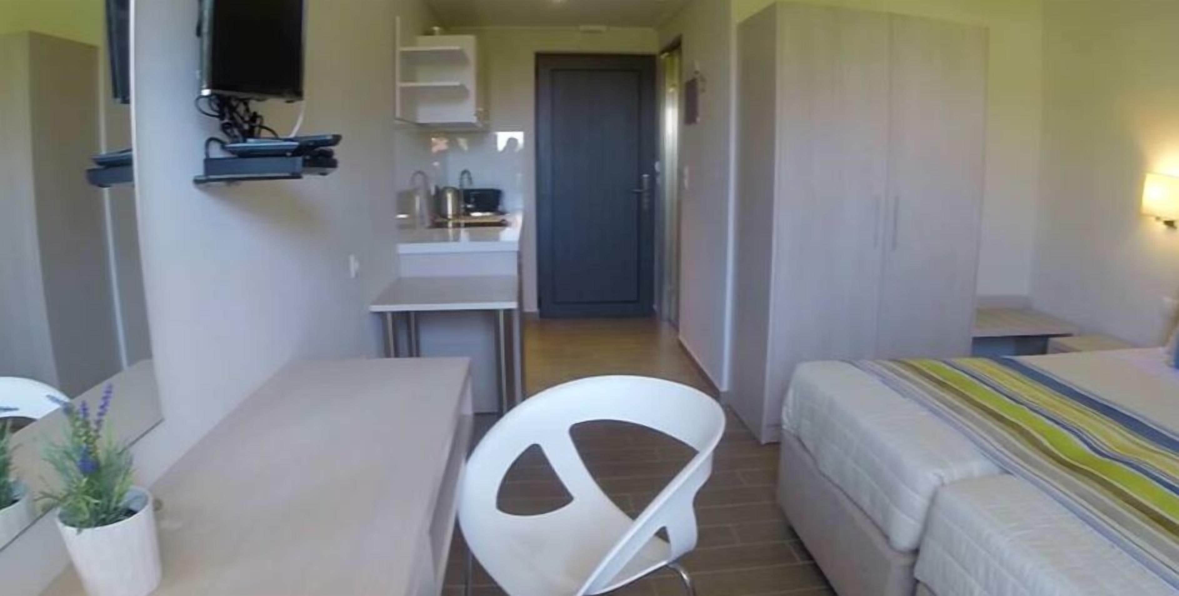 A compact hotel room with a bed, a desk, a chair, and a small kitchenette.