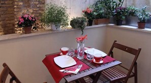 A wooden table set for two with a red tablecloth, white plates, and red cups. There are potted plants on the balcony railing. - Residence Regola (Rome)