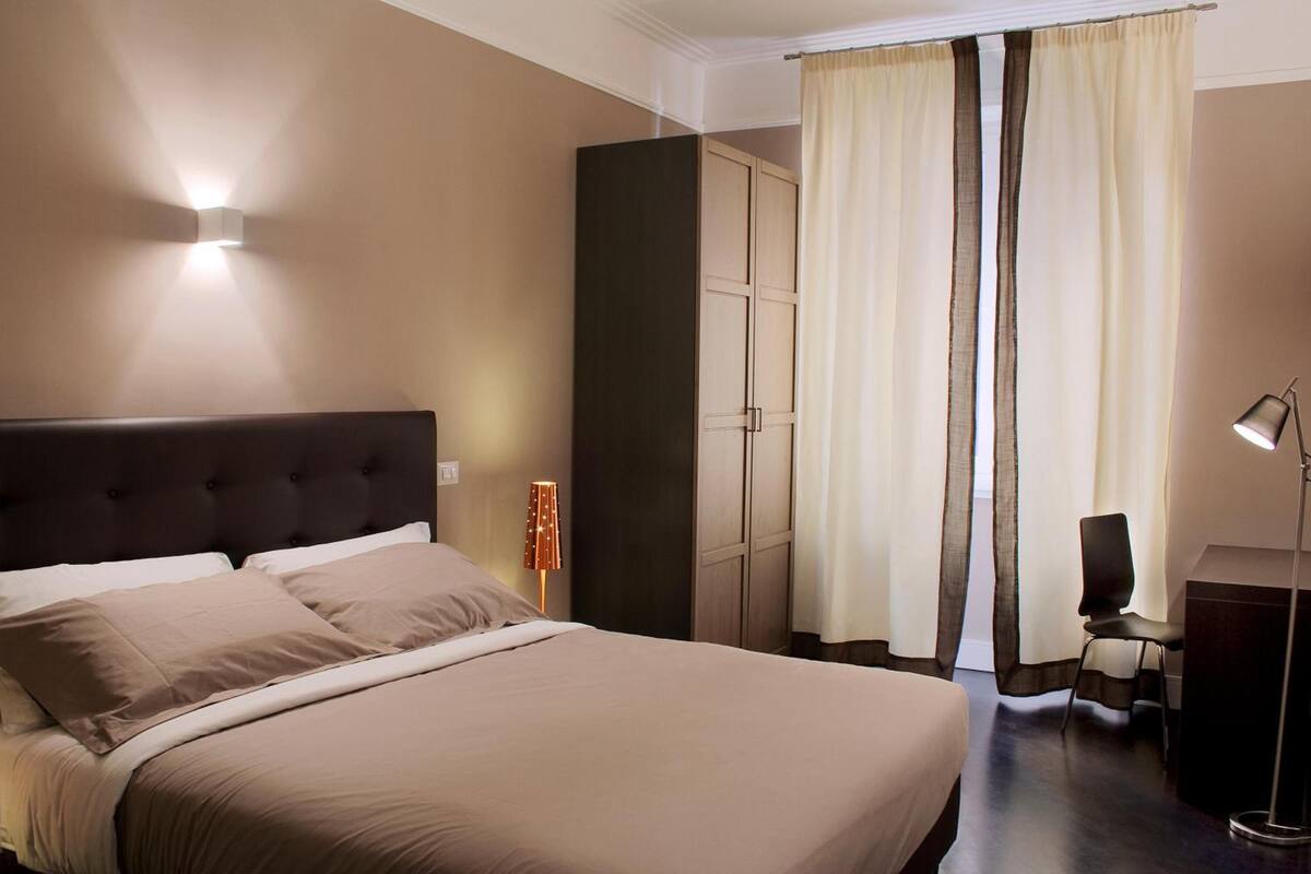 A hotel room with a large bed, a wardrobe, a desk, and a lamp.