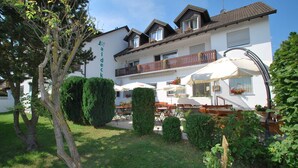 Un hotel con terraza al aire libre, un jardín cuidado y un balcón con plantas en macetas.