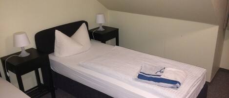 A single bed with white bedding, two bedside tables with lamps, and a dark headboard.