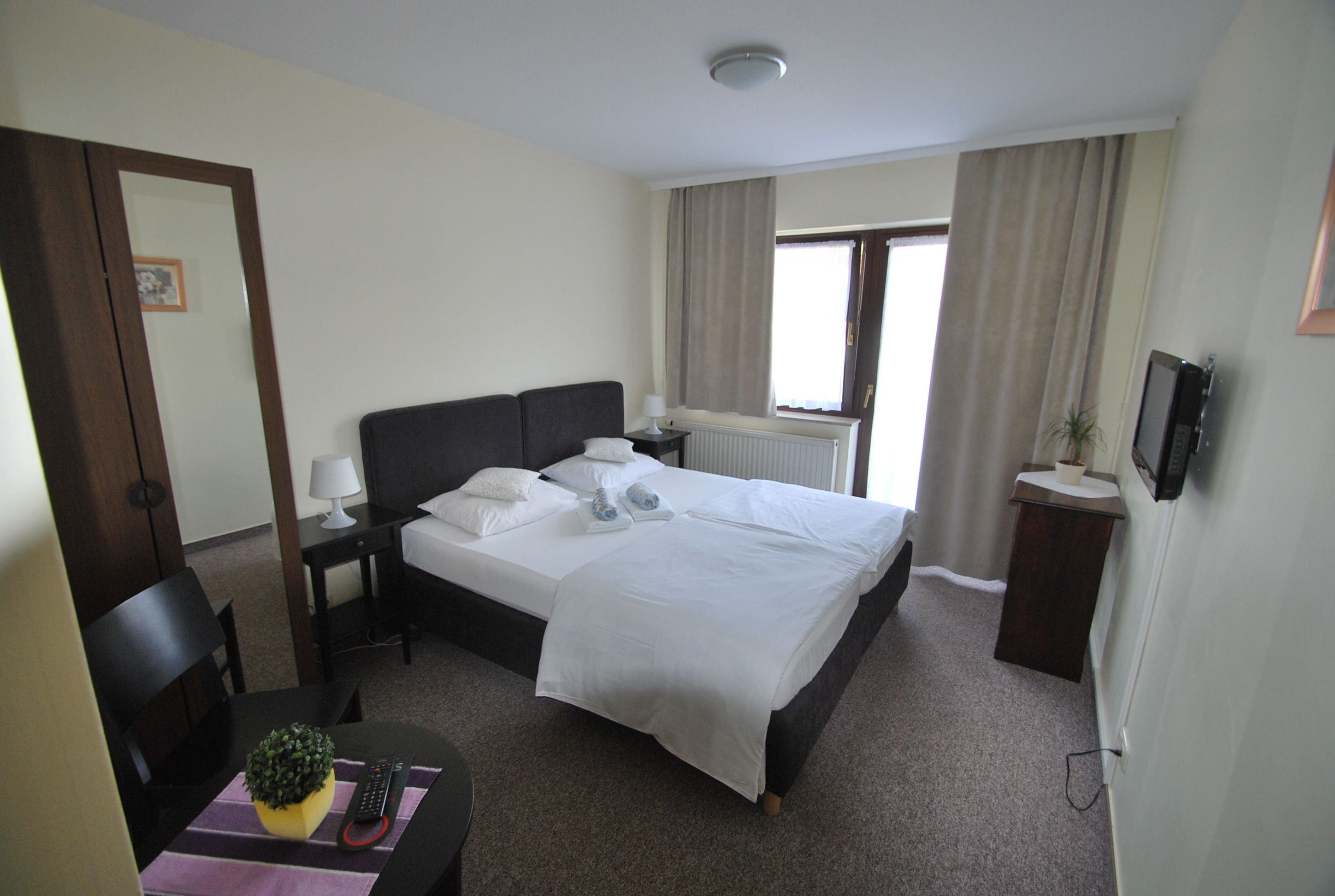 Una habitación de hotel con cama, mesita de noche, lámpara y un pequeño escritorio con una planta.
