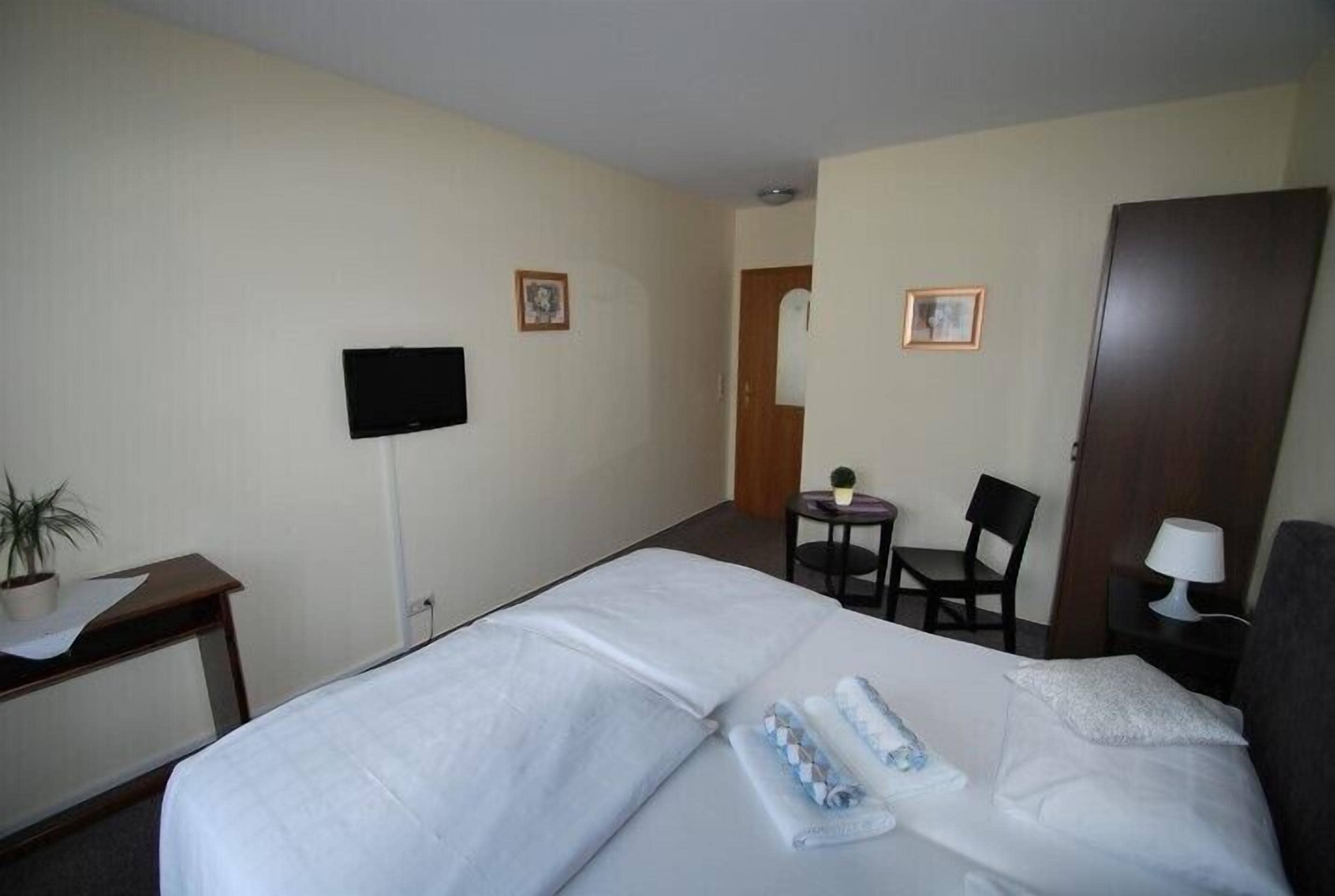 Una habitación de hotel con una cama, un escritorio con una silla, una mesita con una silla, un televisor montado en la pared y una puerta.