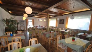 Un restaurante con mesas y sillas de madera, lámparas colgantes y plantas en macetas.