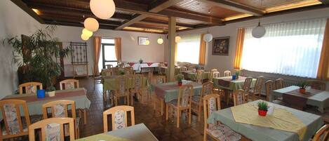 Un restaurante con mesas y sillas de madera, lámparas colgantes y plantas en macetas.