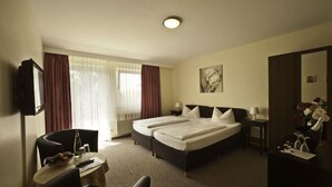 Habitación de hotel con cama doble, un escritorio con silla, televisión y ventana con cortinas.