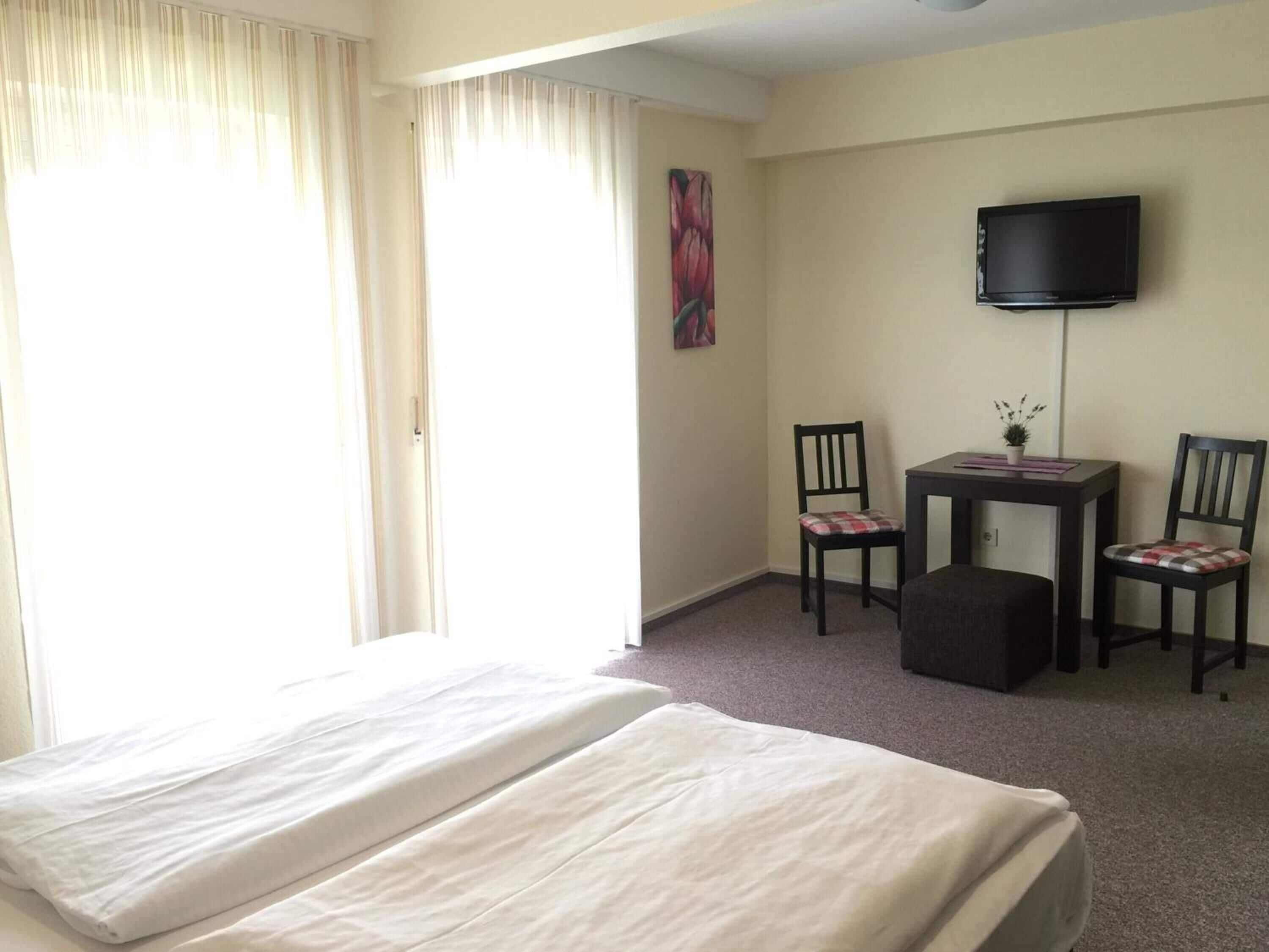 Habitación de hotel con una cama, dos sillones, una mesita, televisor y un cuadro en la pared.