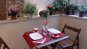 A table set for two with a red tablecloth, two cups, a glass, a vase with a flower, and a wooden chair. - Regola Suite (Rome)