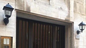 A large, dark metal gate with vertical bars and a central door, flanked by two wall-mounted lanterns and a plaque with a number. - Regola Suite (Rome)