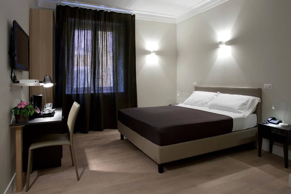 A hotel room with a bed, desk, chair, and a TV.