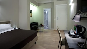 A hotel room with a bed, a desk with a coffee maker, a chair, and a small table with a plant. - Regola Suite (Rome)