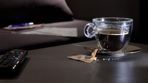 A cup of coffee on a coaster, a remote control, and a lamp on a table. - Regola Suite (Rome)