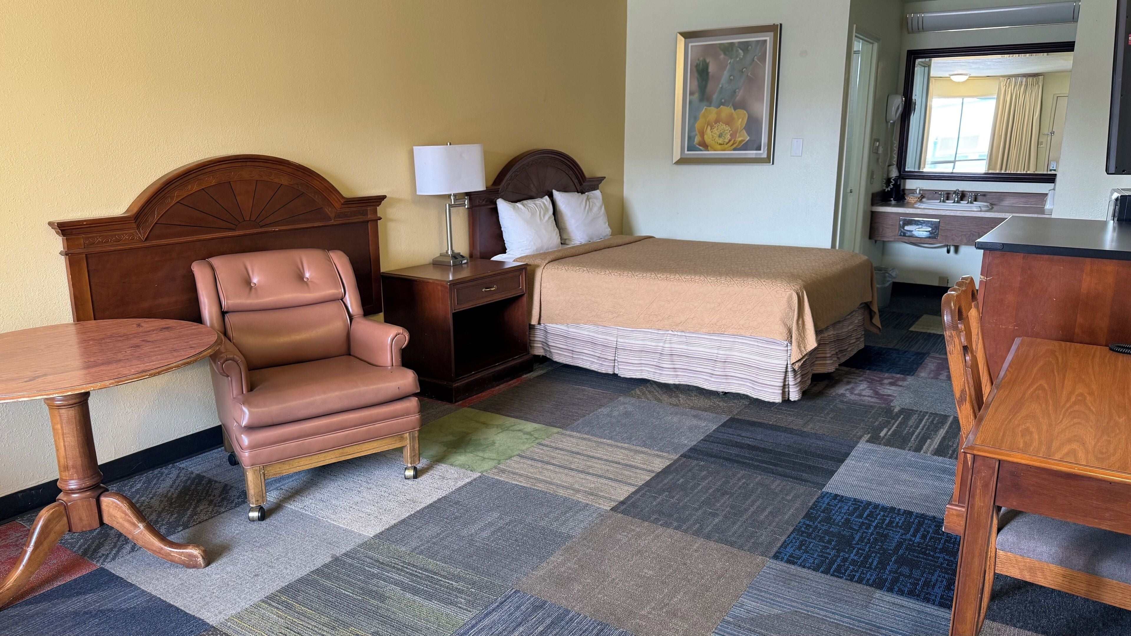 A hotel room with a bed, a chair, a desk, a table, and a bathroom visible through a door.