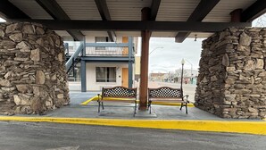 A covered outdoor area with stone walls, two benches, and a building in the background. - Thunderbird Motel (Elko)