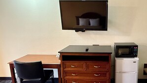 A compact hotel room with a wooden desk, a black chair, a TV mounted on the wall, a microwave, and a small refrigerator. - Thunderbird Motel (Elko)