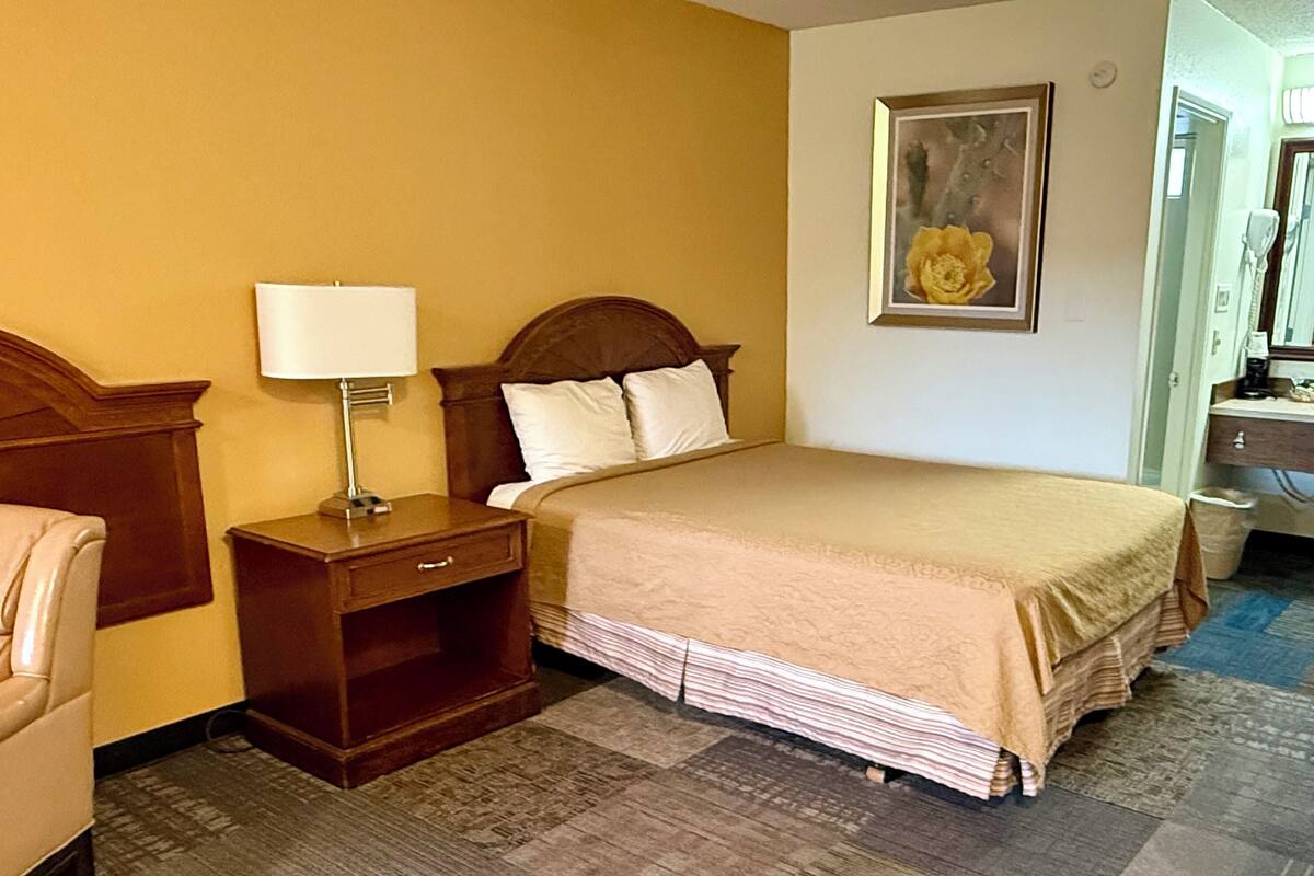 A hotel room with a bed, nightstand, lamp, and a painting on the wall.