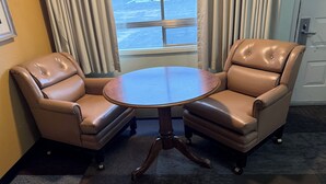 A corner office with two leather chairs, a round wooden table, and a view of the parking lot through large windows. - Thunderbird Motel (Elko)