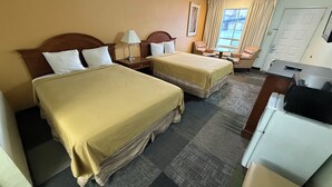 A hotel room with two beds, a desk, a chair, a lamp, and a window with curtains. - Thunderbird Motel (Elko)
