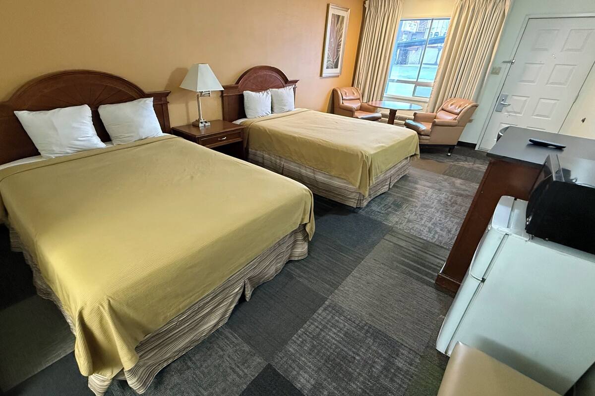 A hotel room with two beds, a desk, a chair, a lamp, and a window with curtains.