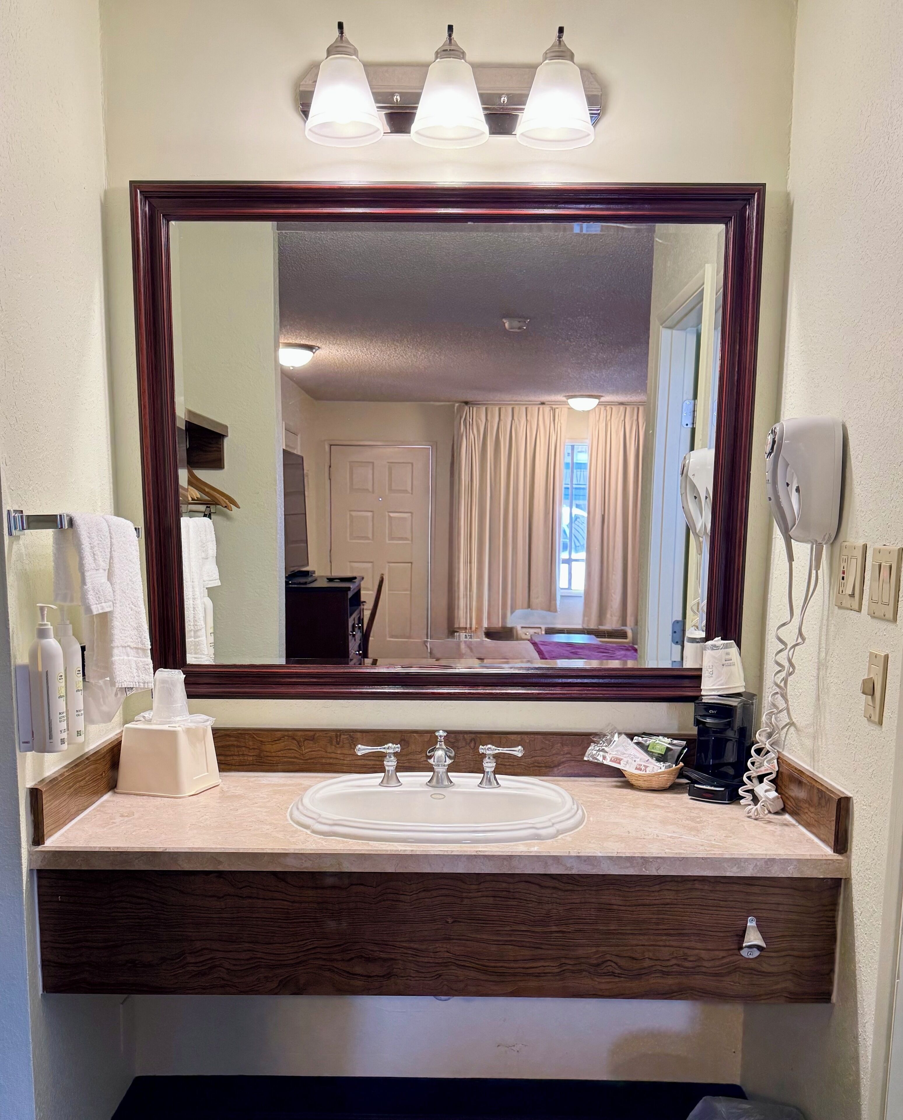 Une salle de bain avec un grand miroir, un lavabo équipé de trois robinets et un sèche-cheveux fixé au mur.