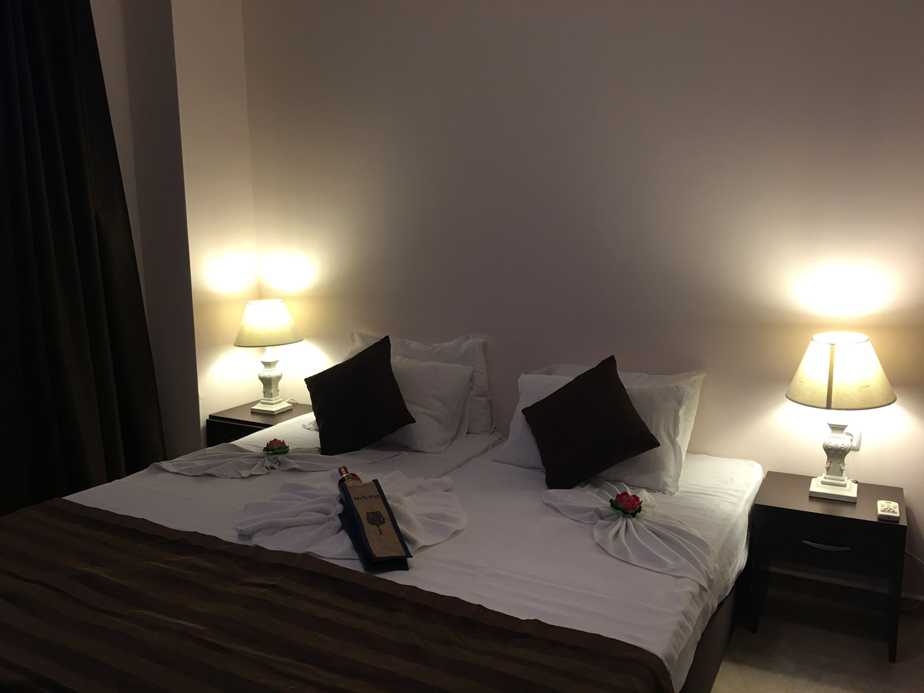 A hotel room with a neatly made bed, two bedside tables with lamps, and a remote control on one of the tables.