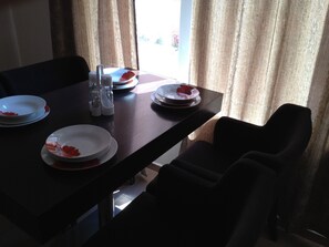 Une table à manger avec des assiettes et des couverts, placée devant une fenêtre ornée de rideaux.