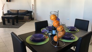 A dining area with a table set for four, featuring green placemats, purple plates, and a decorative metal stand holding oranges.