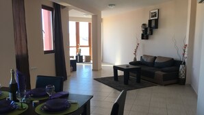 A dining area with a table set for two, a sofa, and a coffee table in a living room.
