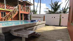 Una piscina con escalones que conducen a ella, rodeada por una terraza de madera y una pared blanca con un letrero que indica una profundidad máxima de 1.32 metros.