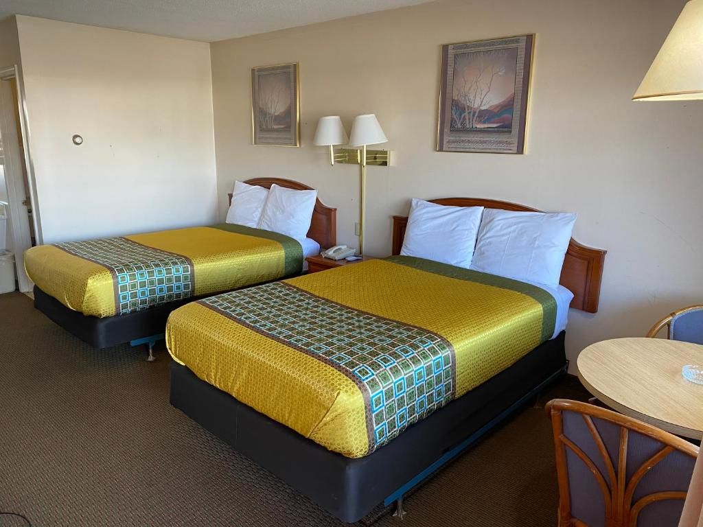 Une chambre d’hôtel avec deux lits, une table de chevet, une lampe et une petite table ronde.
