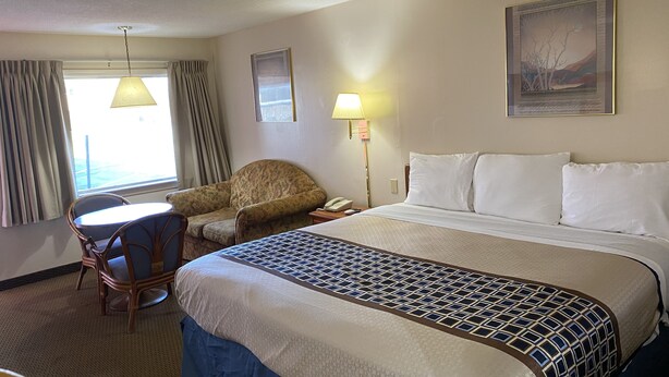 A hotel room with a bed, a chair, a desk, a lamp, and a window with curtains. - Parkview Motel (Corning)
