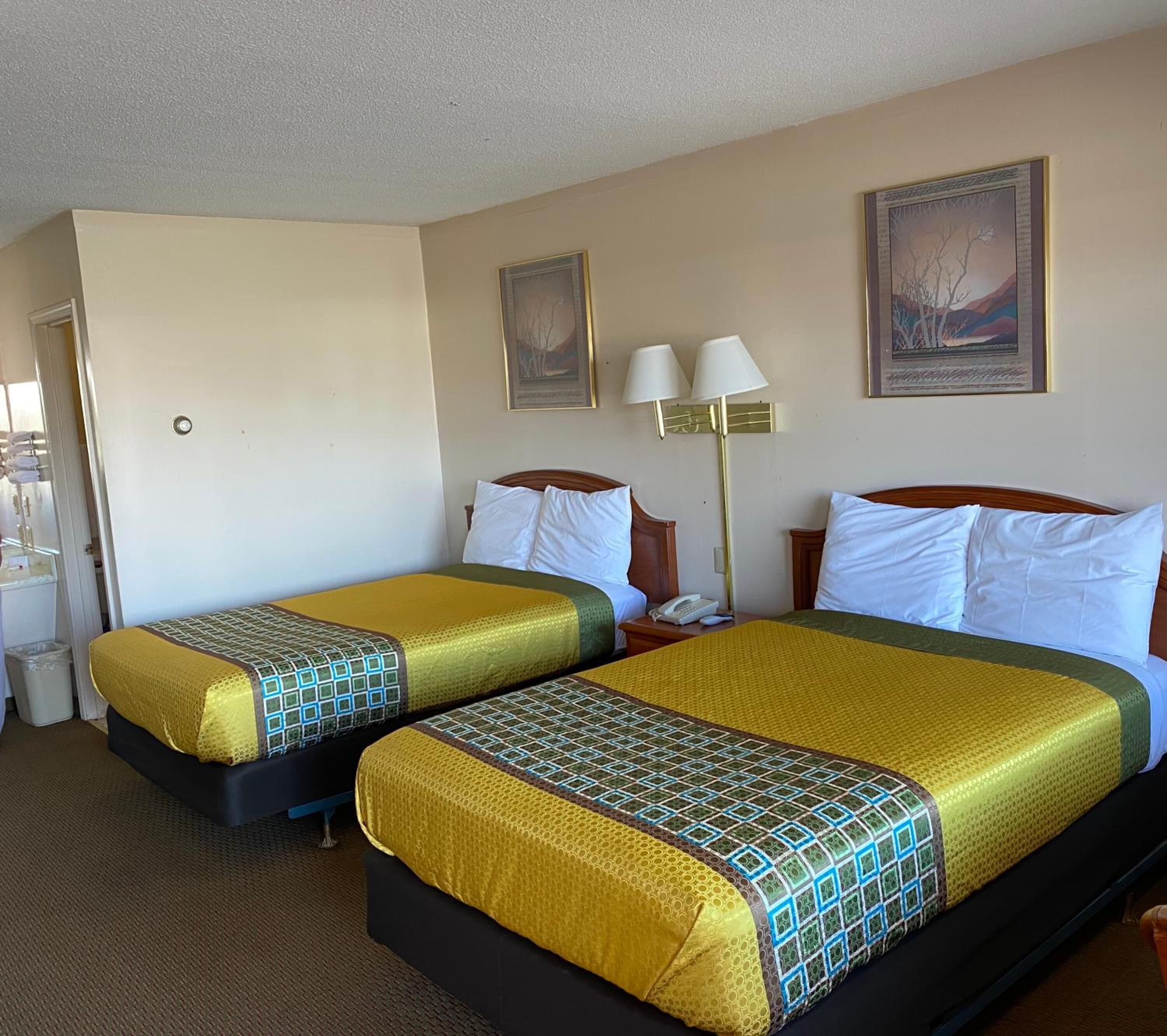 A hotel room with two beds, each with a patterned bedspread, a nightstand with a lamp, and a painting on the wall.
