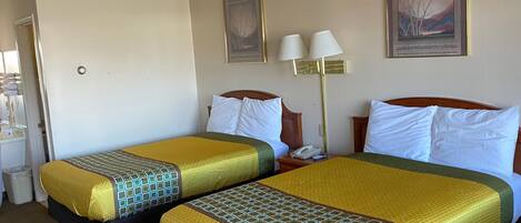 A hotel room with two beds, each with a patterned bedspread, a nightstand with a lamp, and a painting on the wall.