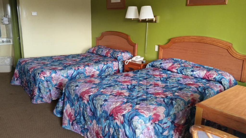 A hotel room with two beds, a bedside table with a lamp, and a wooden chair.