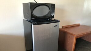 A compact refrigerator with a microwave on top, a small wooden table beside it, and a textured floor. - Parkview Motel (Corning)