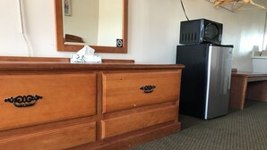 A wooden dresser with a mirror above it, a black refrigerator, and a small table with a cloth. - Parkview Motel (Corning)